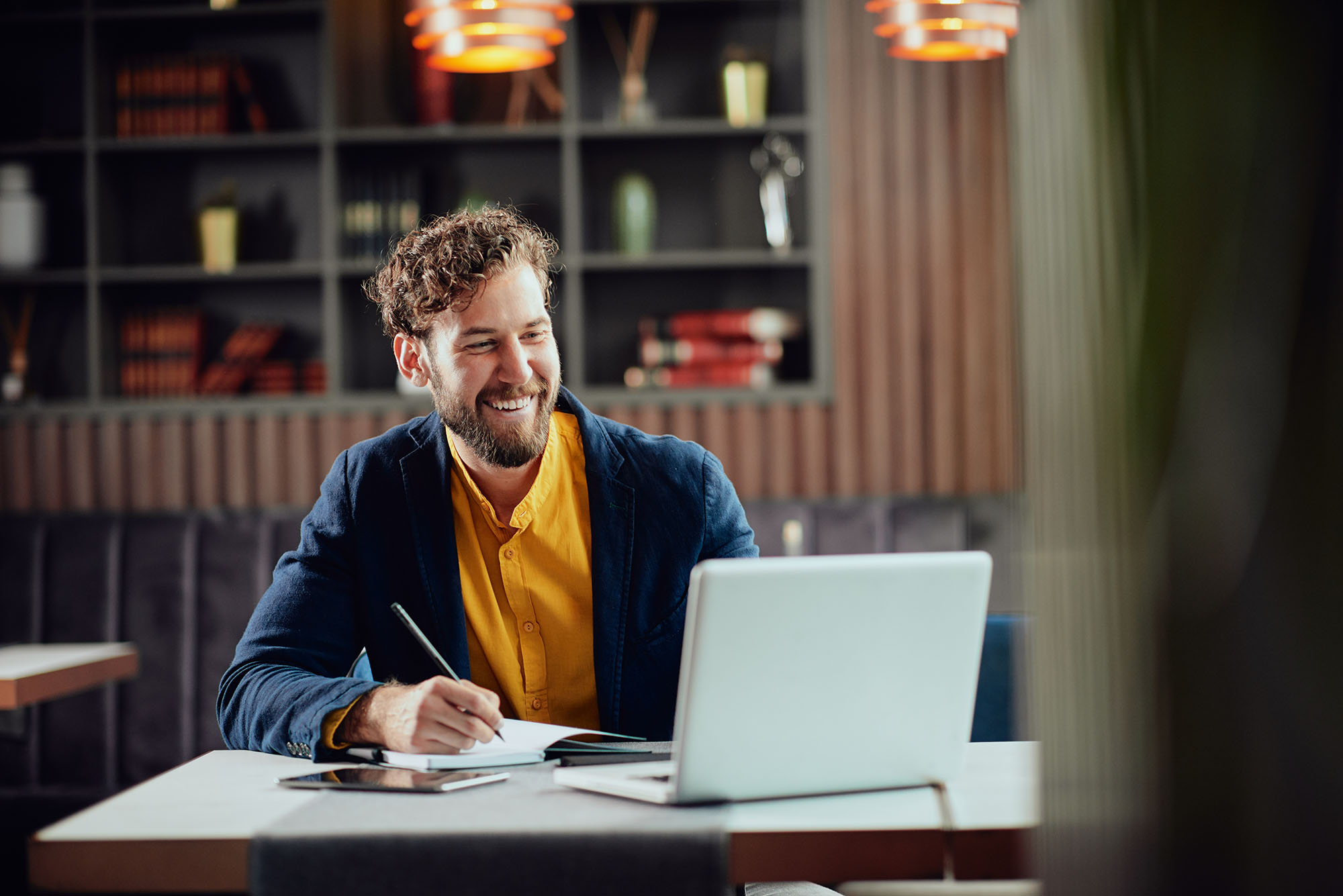 A happy man sat in a quiet space with his laptop, notebook, and pen